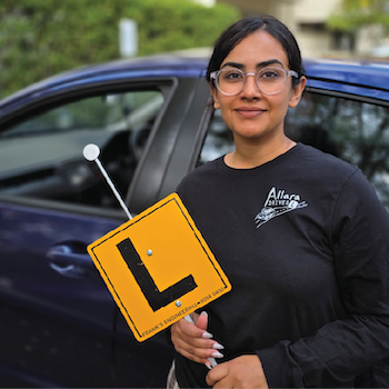 An Allara Drives instructor holding an L-plate sign beside a car.